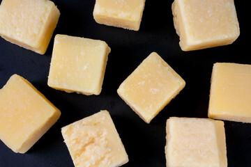 Parmesan cheese cubes on black background. Grana padano hard cheese pieces top view
