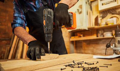 Senior carpenter with drilling instrument working in the carpentry workshop to make a piece of...
