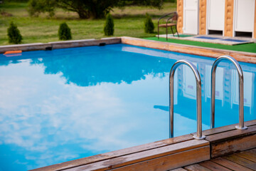 Ladder stainless handrails for descent into swimming pool.Metal Handrails and blue water at sunset. Swimming and summer rest concept.pool with stair and wooden deck.copy space