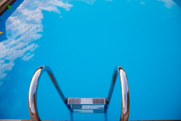 Ladder stainless handrails for descent into swimming pool.Metal Handrails and blue water at sunset....