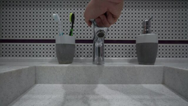 Person hand open tap and water flows to stone sink at bathroom of apartment or hotel room. Thrift and saving concept.