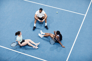Minimal high angle at group of people relaxing at indoor tennis court and sitting on graphic blue...