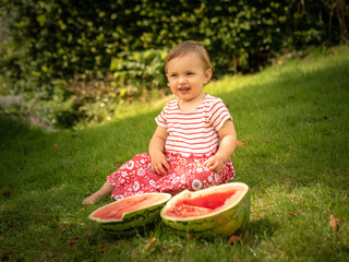 A one year old baby girl is eating fresh watermelon on a sunny day on her summer holidays at the countryside in a cottage in England