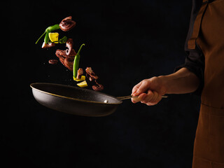 Cooking seafood, octopus with lemon slices and vegetables in a frying pan on a black background....