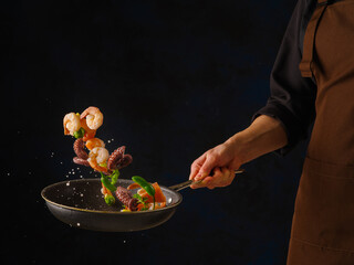 Seafood with vegetables and herbs in a frying pan on a black background in the chef's hand....