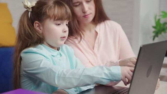 Child, girl studies at home at computer with teacher. Teamwork handshake. Homeschooling, mom, smart kid daughter, laptop. Family school, daughter does homework at table, teacher helps. Happy family