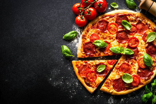 Pizza on black background. Traditional italian pizza with salami cheese, tomatoes and basil. Top view with copy space.