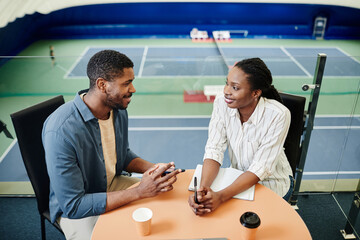 High angle portrait of smiling black sportsman talking to female coach during after practice...