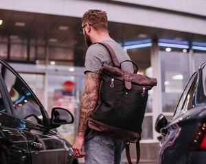 Handsome man with close up canvas and leather backpack. Rear view