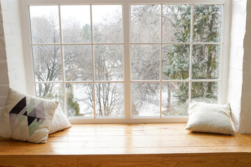 Сozy and frost winter still life, white pillows on windowsill against snow landscape from outside