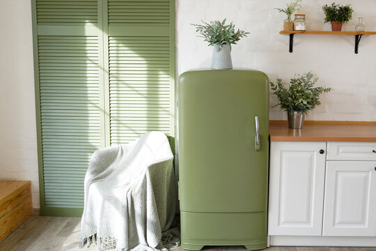 Bright Green Kitchen Interior With Wooden Floor, White Furniture, Shelves And Houseplants In Pots