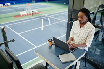 High angle portrait of young black businesswoman using laptop while working in sports training...