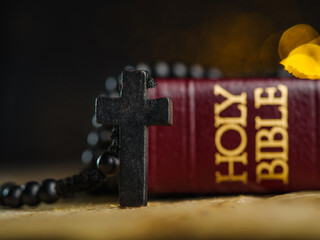 Catholic cross on the rosary. Holy bible book on wooden table against dark background. There are no...