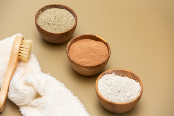Organic green, red, white face mask clay in wooden bowls with soft sponge bandage and bamboo and goat hair brush on beige background. Home skin care concept.Self care