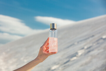 Woman hold in hand bottle with oil on white dune background