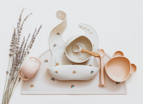 Flat lay composition with silicone set tableware for baby, bibs and plate on beige background. Serving food. Concept of kids menu, nutrition and feeding