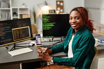 Portrait of female IT developer looking at camera and smiling against programming code on computer...