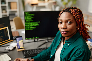 Portrait of young female IT developer looking at camera against programming code on computer screen...