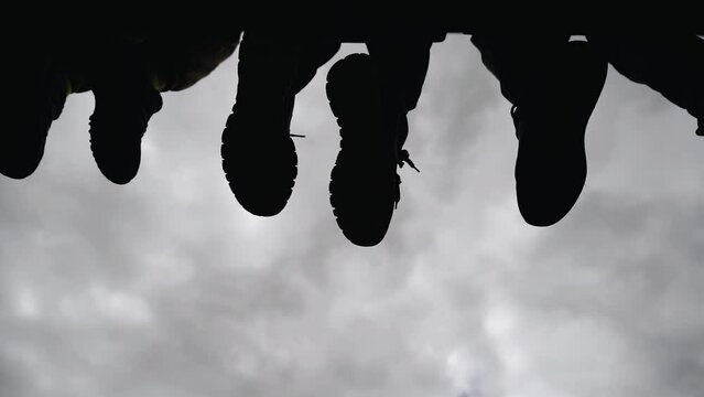 Children sit on the edge of the ledge with their legs hanging down, relaxed. Silhouettes of legs against the sky