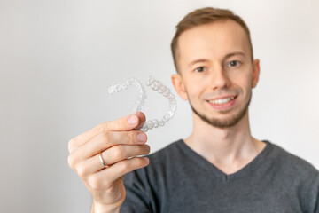 Young handsome man holding dental aligner tooth correction over white background
