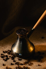 An old copper cezve stands on a dark background. Coffee beans are scattered on burlap.