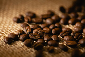 Close-up of a scattering of coffee beans on a dark burlap background.