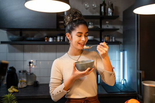 One young caucasian woman having breakfast in the kitchen at home female adult eating in her apartment while standing having healthy vegan meal muesly or oatmeal happy smile real people copy space