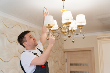 A male electrician changes the light bulbs in the ceiling light. 
