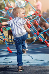 Cute preschool boy having fun on outdoor playground. Summer active sport leisure for kids.Equipment of entertainment park for kids. The child is ready to climb the rope tower