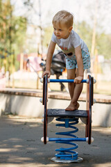 The brave little boy stands up and balances on a spring swing on the playground
