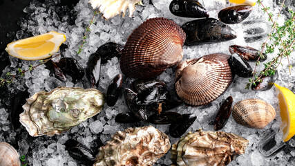 Raw oysters and mussels on ice on black slate. Fresh Clams in whole shells for cooking with seasonings on the table, close up © Andrey