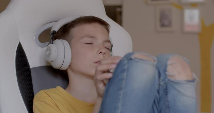 Teenager in noise canceling headphones is spinning in an armchair at home. Help kids on autism and ADHD and sensory processing disorder cope with loud sounds. CZ, Kladno, Polska, 16.4.2022