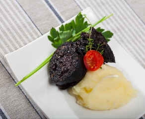 Fried morcilla (blood sausage with rice) served on white plate with pureed potatoes, tomatoes and...