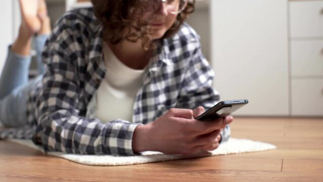 Girl schoolboy studen lies on the floor with a phone in her hands. Hands holding a modern smartphone typing text to send an email. Leisure time. Rest break answer in social networks
