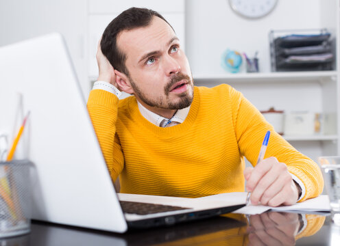 Man In Yellow Shirt At Office Of Serious Documents On Laptop Computer