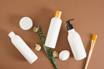 three different mockup bottles for cosmetics, a brush, a jar, leaves and quail eggs on a brown background