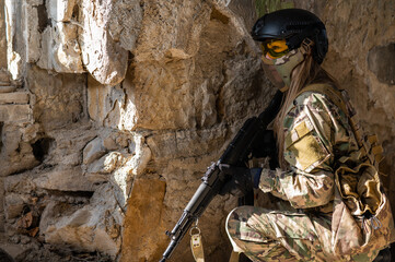Portrait of a woman in a helmet and goggles with a machine gun in her hands. A female soldier in a...