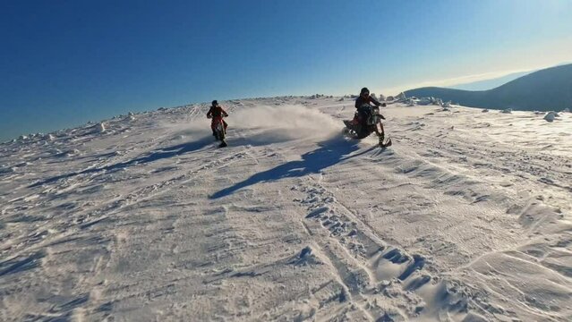 Beautiful aerial top view in mountains, two guys on snowmobile jumps and rides in the winter at sunlight