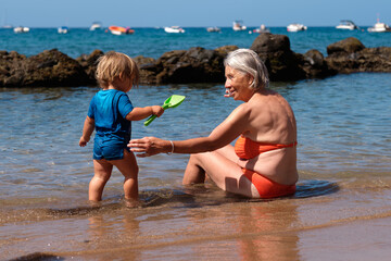Grandmother sitting by the sea with her grandson. Woman. Older woman on vacation with her grandson.