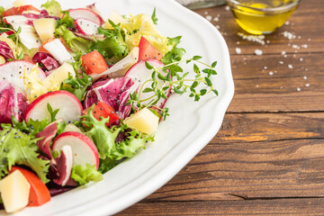Fresh salad with mixed greens, radish, cheese and tomato in a plate on wooden background. Italian Mediterranean or Greek cuisine. Vegetarian vegan food.