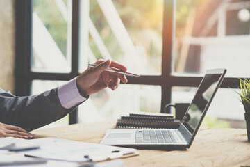 Business man hold stylus pen and pointing to laptop at office with document report, graph,...