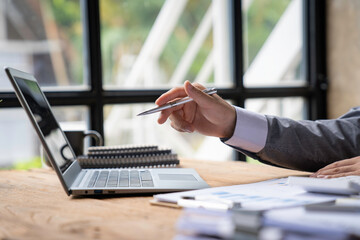 Business man hold stylus pen and pointing to laptop at office with document report, graph,...