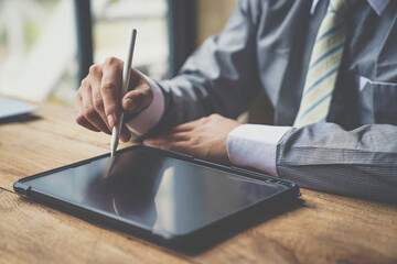 Man working contemporary electronic tablet while sitting at the wooden table at office.Men using...