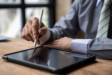 Man working contemporary electronic tablet while sitting at the wooden table at office.Men using...