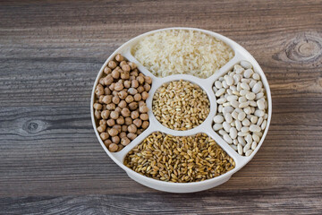 Uncooked dried chickpeas, wheat, rice and white beans in divided plate on wooden surface