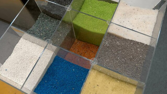 In glass square containers, samples of plastic granules of different colors for the production of plastic items by extrusion. Closeup. Shot in motion