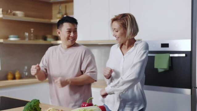 Footage of good-looking young international couple spending time on kitchen at home. Synchronized movements. Happy young multi ethnic couple in love dancing. Attractive Caucasian woman and handsome
