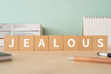 嫉妬のイメージ｜「JEALOUS」と書かれた積み木が置かれたデスク
