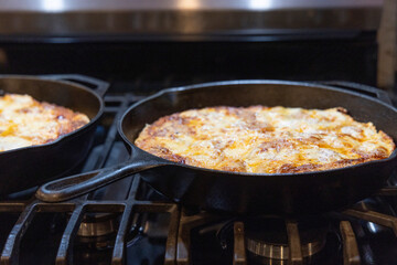 Two homemade pizzas of peperoni and cheese are fresh from cooking in cast iron skillets and ready to be served. 