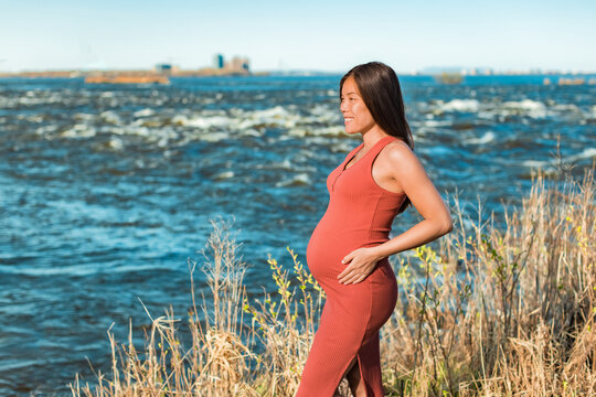 Maternity portrait of Asian woman during pregnancy holding pregnant belly against nature river background. Outdoor walk in natural environment